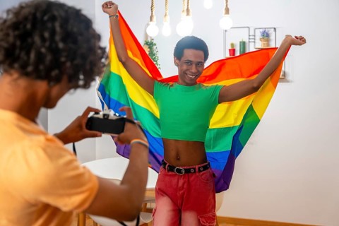 Gay man posing sensual with LGBT flag at home with his partner taking photos