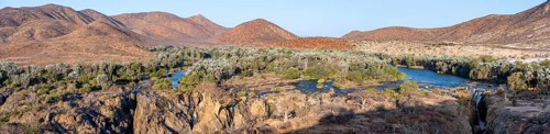 Panorama, Kunene River with green vegetation in dry red mountain landscape, waterfall and African