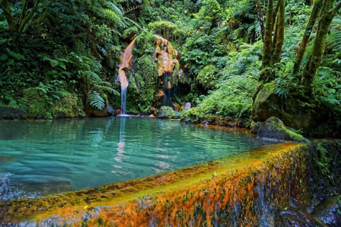 Turquoise-coloured thermal spring with waterfall, surrounded by lush vegetation and ferns, Caldeira
