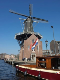 A traditional windmill with a Dutch house in the foreground, next to a quiet canal, Haarlem,