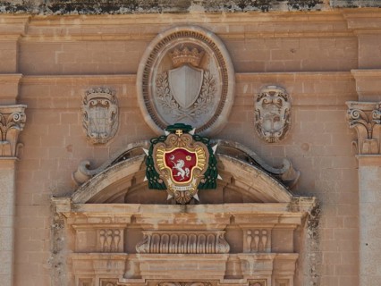A detailed coat of arms on an old stone wall, surrounded by ornaments and reliefs, the town of