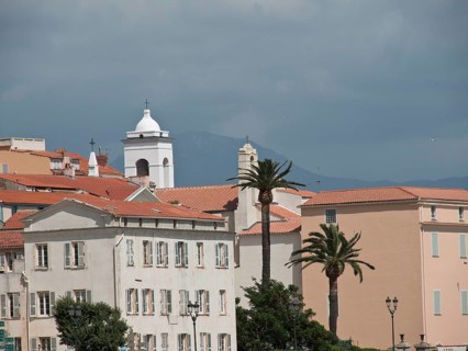 Mediterranean town with white buildings, a church tower and palm trees against a cloudy sky and