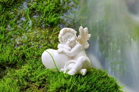 Porcelain angel figurine on moss by a waterfall