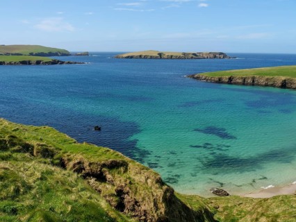 Turquoise waters meet rocky cliffs and green grasslands under a blue sky, Green meadows by the sea