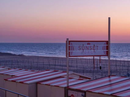 A sign with the inscription 'Sunset Beach' above the beach huts at sunset, sunset in many colours