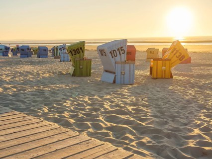 Several colourful beach chairs standing in order in the sand while the sun illuminates the horizon,