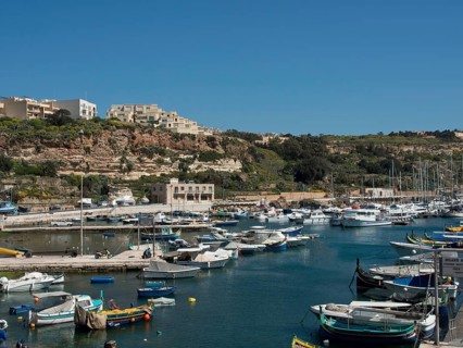 A quiet harbour with many sailing ships and fishing boats, surrounded by a hilly coastline and