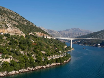 Landscape with coastal road and a bridge over a wide river, surrounded by green hills, the old town