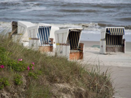 White beach chairs with blue and white stripes stand near the dunes by the sea with waves, beach