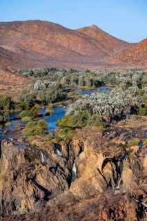 Kunene River with green vegetation in dry red mountain landscape, waterfall and African Baobab
