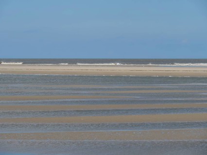 Empty beach at low tide with strips of sand and water under a blue sky, Baltrum Germany
