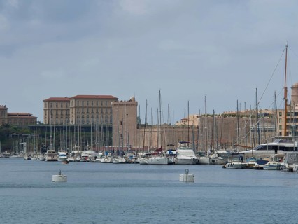 A harbour full of boats and yachts with historic buildings and sailing masts in the background,