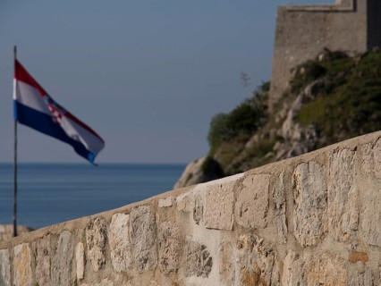 Croatian flag flying next to a historic fortress, overlooking the sea and the clear blue sky, the