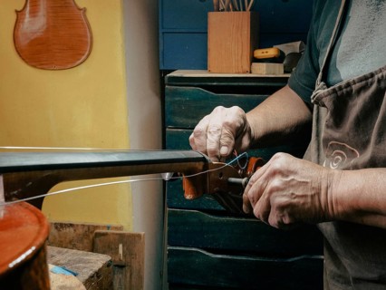 A luthier works on a cello strings in a workshop, focusing intently on string adjustments