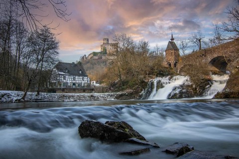 Beautiful landscape in winter with ice and snow. Waterfall of the river Elz near the castle