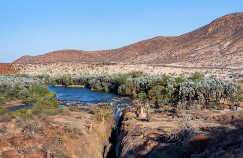 Kunene River with green vegetation in dry red mountain landscape, waterfall and African Baobab