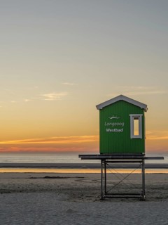 Sunset over the sea with green lifeguard tower on the beach, setting sun on the North Sea beach