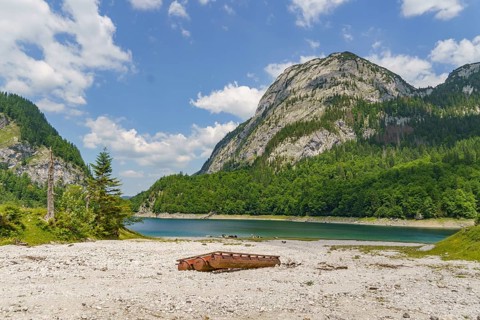 Rusted piece of metal on the shore of a lake with mountains in the background, turquoise green