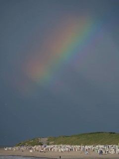 A rainbow appears in the dark sky above a beach, Baltrum Germany
