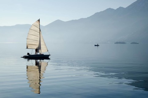 Old Sailing Boat Reflected on Lake Maggiore with Brissago Islands and Mountains in a Misty Sunny