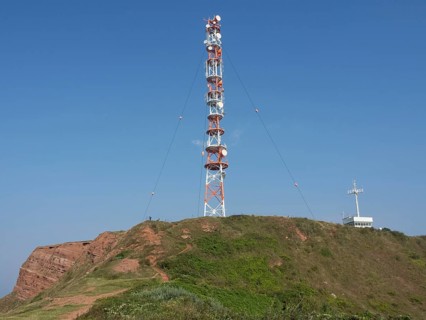 A large transmission mast stands on an overgrown hill under a clear sky. A technical highlight in