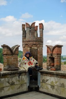 Contemplative older woman sits on a brick balcony overlooking a lush landscape, her expression