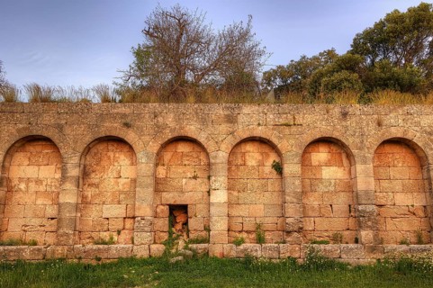 Next to amphitheatre, Ancient stone wall with several arches surrounded by vegetation and peaceful