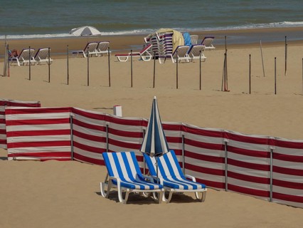 Empty beach with scattered blue and white striped deckchairs, parasols, red partitions and sea