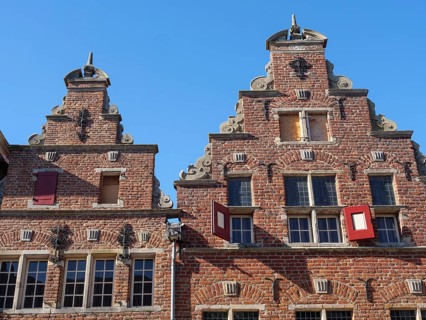 Historic red brick buildings with ornate facades and turrets under a clear blue sky, red brick