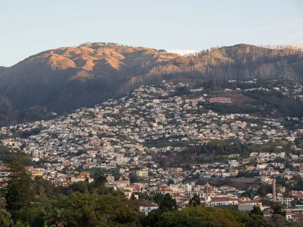 A hilly urban landscape with densely populated houses along the mountain slopes at sunset, Madeira,