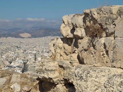 Large ancient stones on a hill overlooking a modern city under a blue sky, Ancient buildings with
