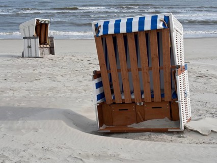 Empty beach chairs on the sandy beach with a view of the calm sea and the slightly cloudy sky,