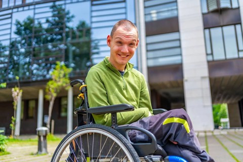 Happy disabled caucasian adult man in wheelchair smiling at camera outside the university
