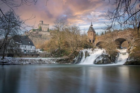 Beautiful landscape in winter with ice and snow. Waterfall of the river Elz near the castle