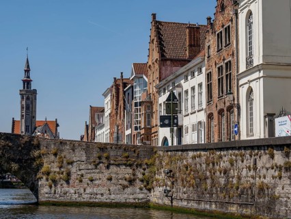 Stone bridge and historic facades with a view of a church tower along a canal under a blue sky,