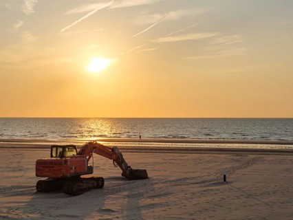 A dredger in warm light on the beach during sunset, facing the calm sea, sunset on the beach of de