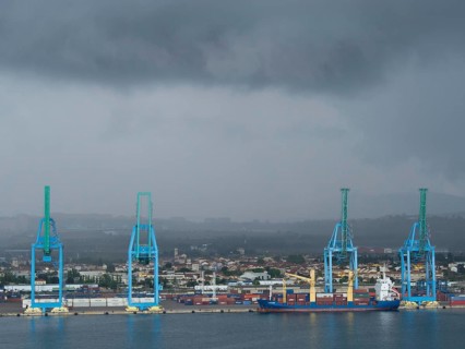 Large blue harbour cranes lifting containers, cloudy sky and a ship in the harbour industrial area
