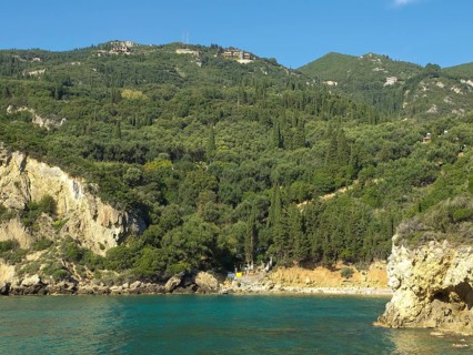 Lush hills stretch down to the coast with clear blue water and a small beach, beach on the island
