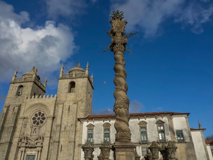 Gothic cathedral with a spiral column in the foreground under a clear blue sky, old houses in the