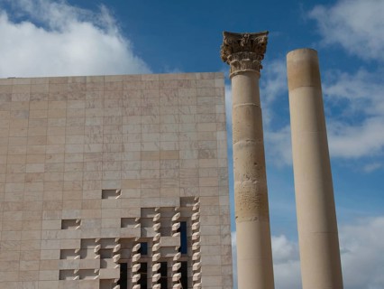 Two columns in front of a modern building with a fragment of ancient architecture and a heavenly