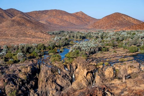Kunene River with green vegetation in dry red mountain landscape, waterfall and African Baobab