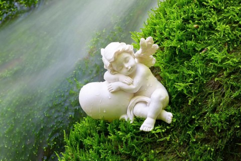 Porcelain angel figurine on moss by a waterfall
