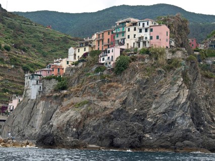 A village of colourful little houses clings to a rocky coastline surrounded by green hills, Bari,