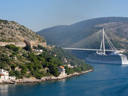 View of a coastline with green hills, a bridge and a cruise ship under a clear blue sky, the old