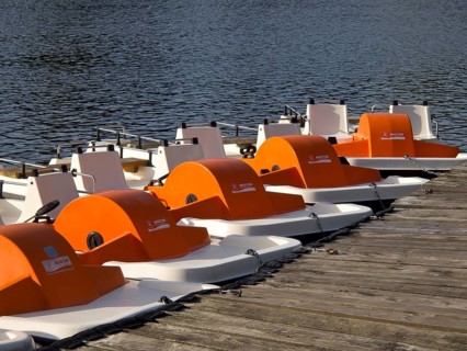 Row of orange-coloured pedal boats along a wooden jetty at the lake, small lake with hiking trails