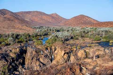 Kunene River with green vegetation in dry red mountain landscape, waterfall and African Baobab