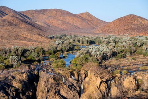 Kunene River with green vegetation in dry red mountain landscape, waterfall and African Baobab