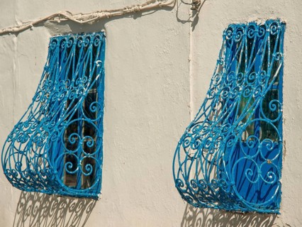 Two windows with decorative blue metal grilles on a light-coloured wall, Tunis in Africa with ruins