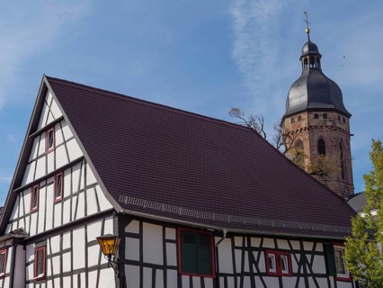 A half-timbered house with red roof tiles next to a gothic church with a tower under a blue sky,