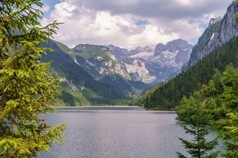 Spectacular lake surrounded by steep mountains and dense forest under a cloudy sky, turquoise green